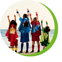 Vier Kinder am Strand mit hochgereckten Fäusten, tragen bunte Superhelden-Capes und Sportkleidung